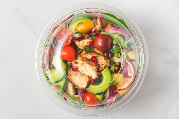 Plastic package with healthy chicken salad with avocado , tomatoes and pomegranate to take away. top view